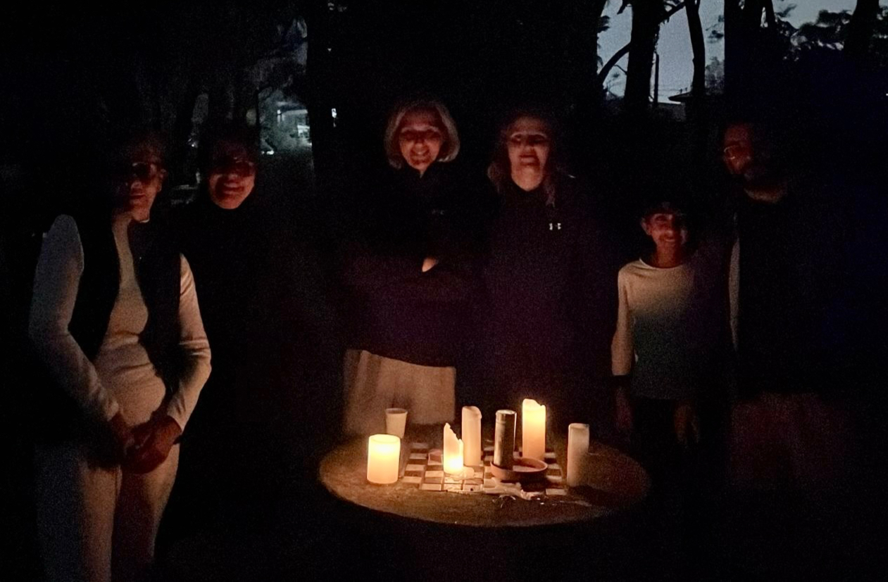 Moradores ao redor de uma mesa à noite, com velas acesas em uma praça do bairro sem iluminação.